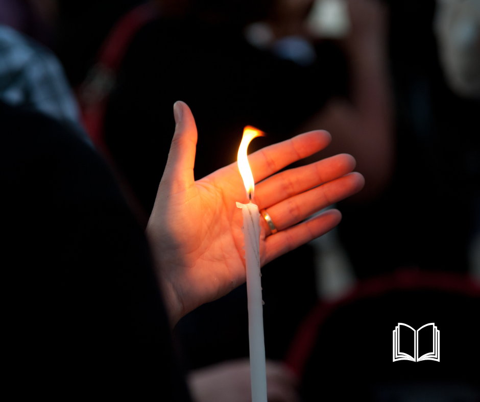A lit candle with a woman's hand shielding the flame.