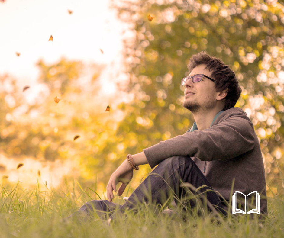 A young man sitting in a sunny field looking at the sky.