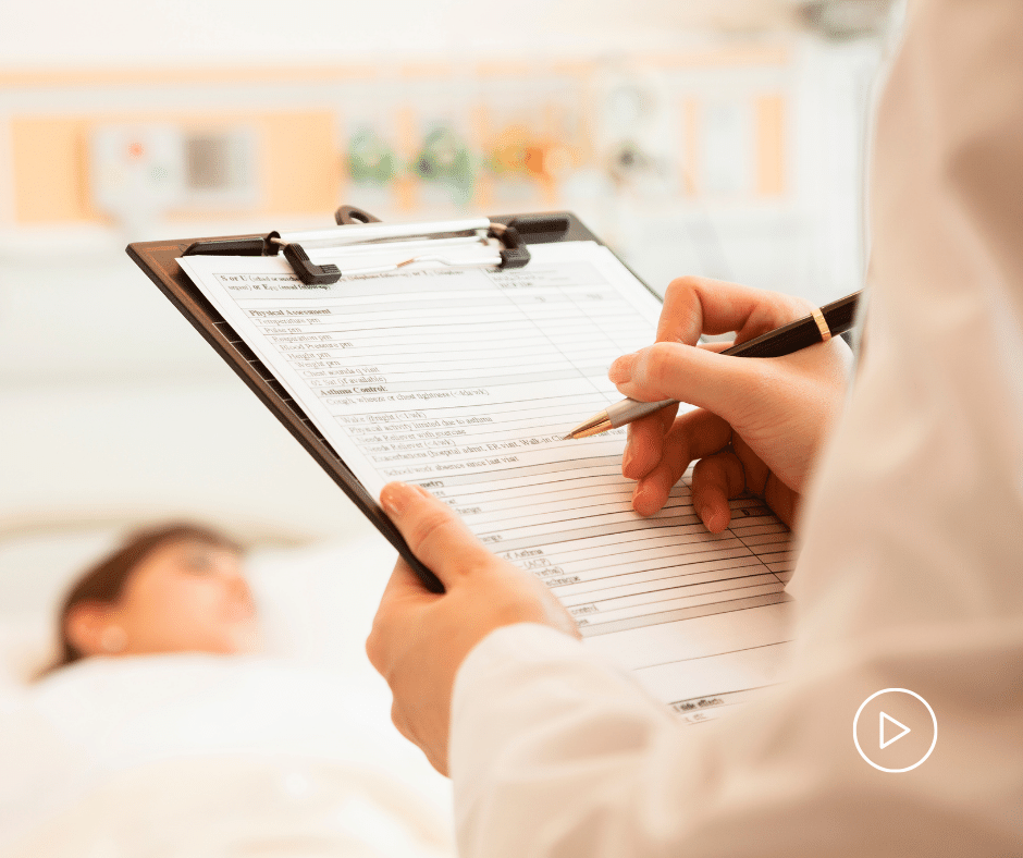 Patient lying in bed, with a doctor's hands writing in their patient's chart.