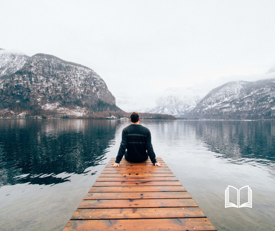 Back of male figure at the end of a dock, overlooking the snow-capped mountains and ocean.