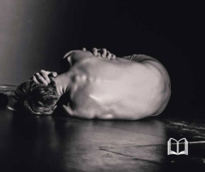 Figure curled in a fetal position on the floor in a dark room.
