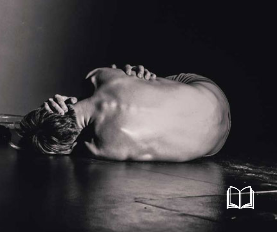 Figure curled in a fetal position on the floor in a dark room.