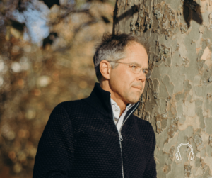 Prof Dr. Jan Bonhoeffer leaning against a tree during a sunny day.