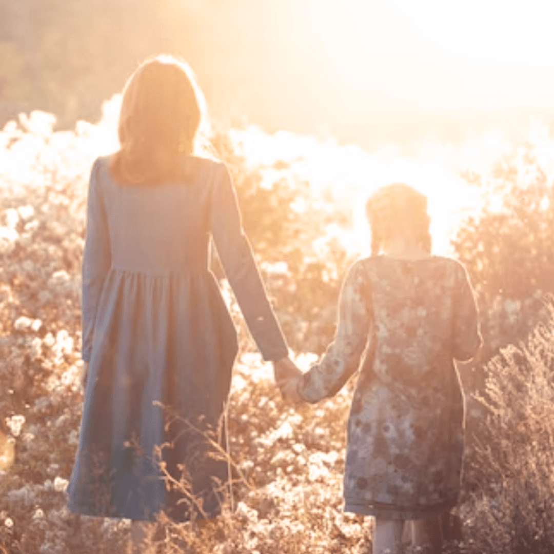 Two female children holding hands in a flower field.